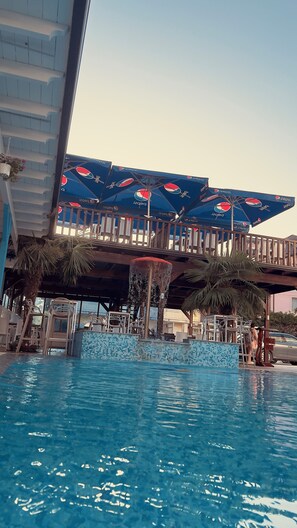 A swimming pool with a tiled edge, umbrellas with Pepsi branding, and a wooden deck above. - Hotel Brian  (Velipoje)