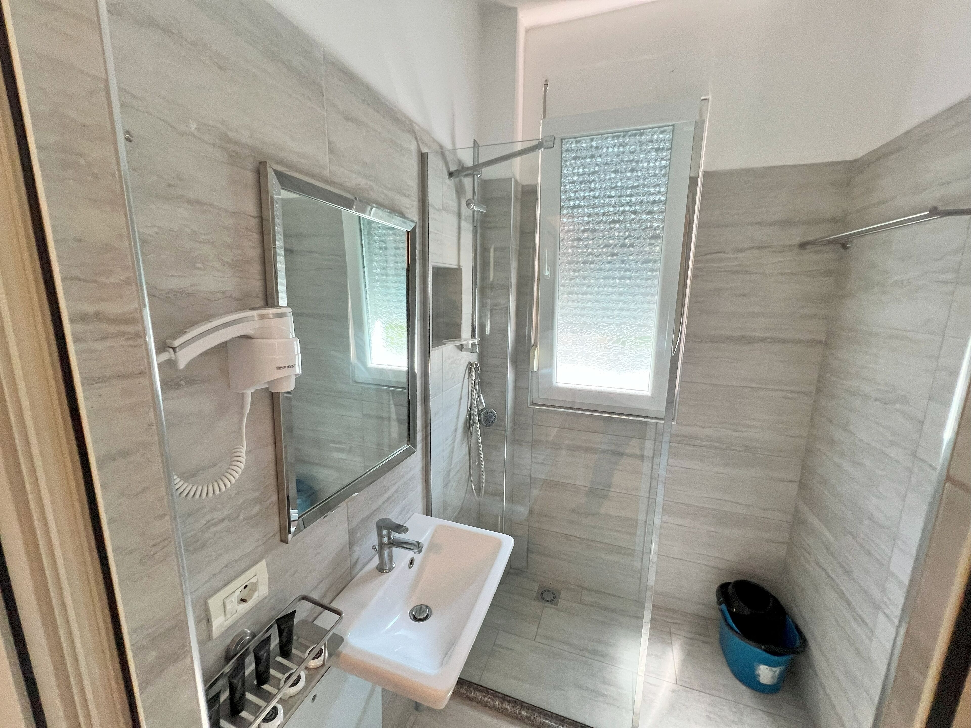 A modern bathroom with a glass shower enclosure, a sink with a mirror, and a hairdryer mounted on the wall.