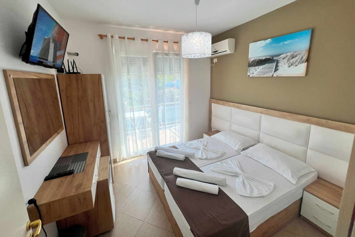A hotel room with a bed, a desk, a television, and a painting on the wall.