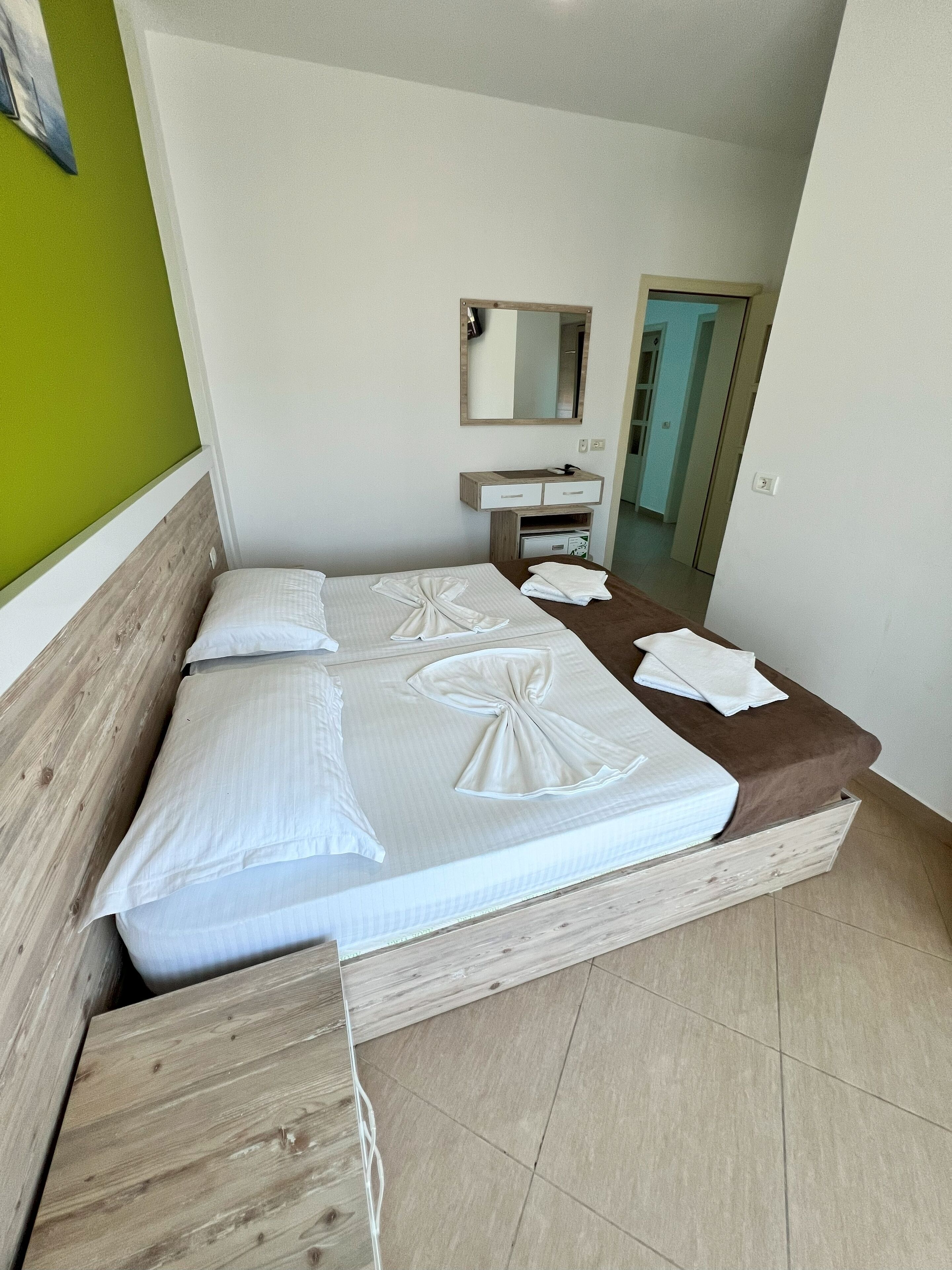 A hotel room with a bed, a bedside table, a mirror, and a green wall.