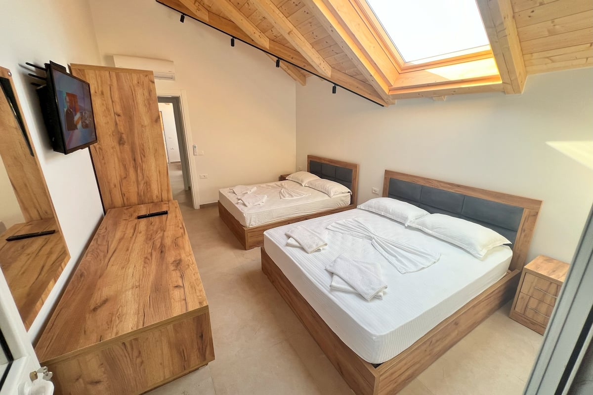 A bedroom with two beds, wooden furniture, a skylight, and a TV on the wall.