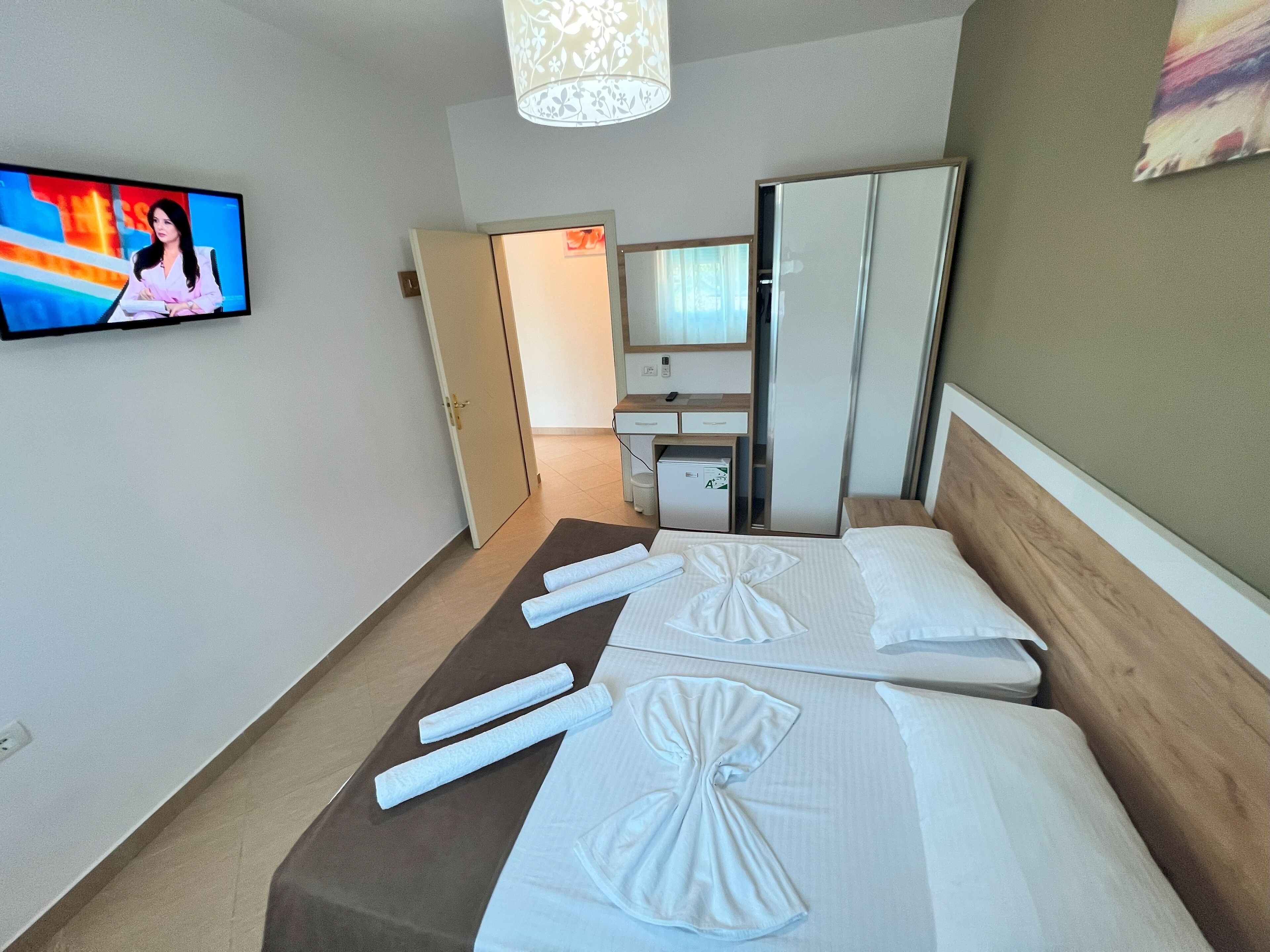 A hotel room with two beds, a TV, a desk, a wardrobe, and a small fridge.