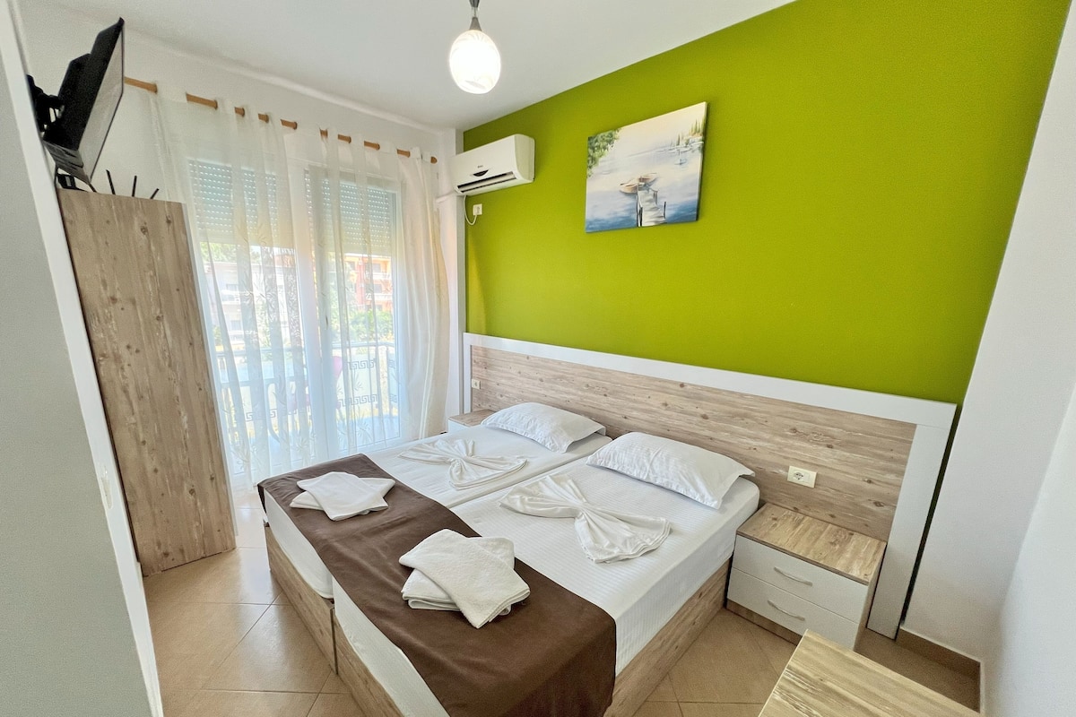 A hotel room with a bed, a wooden wardrobe, a green wall, and a painting.