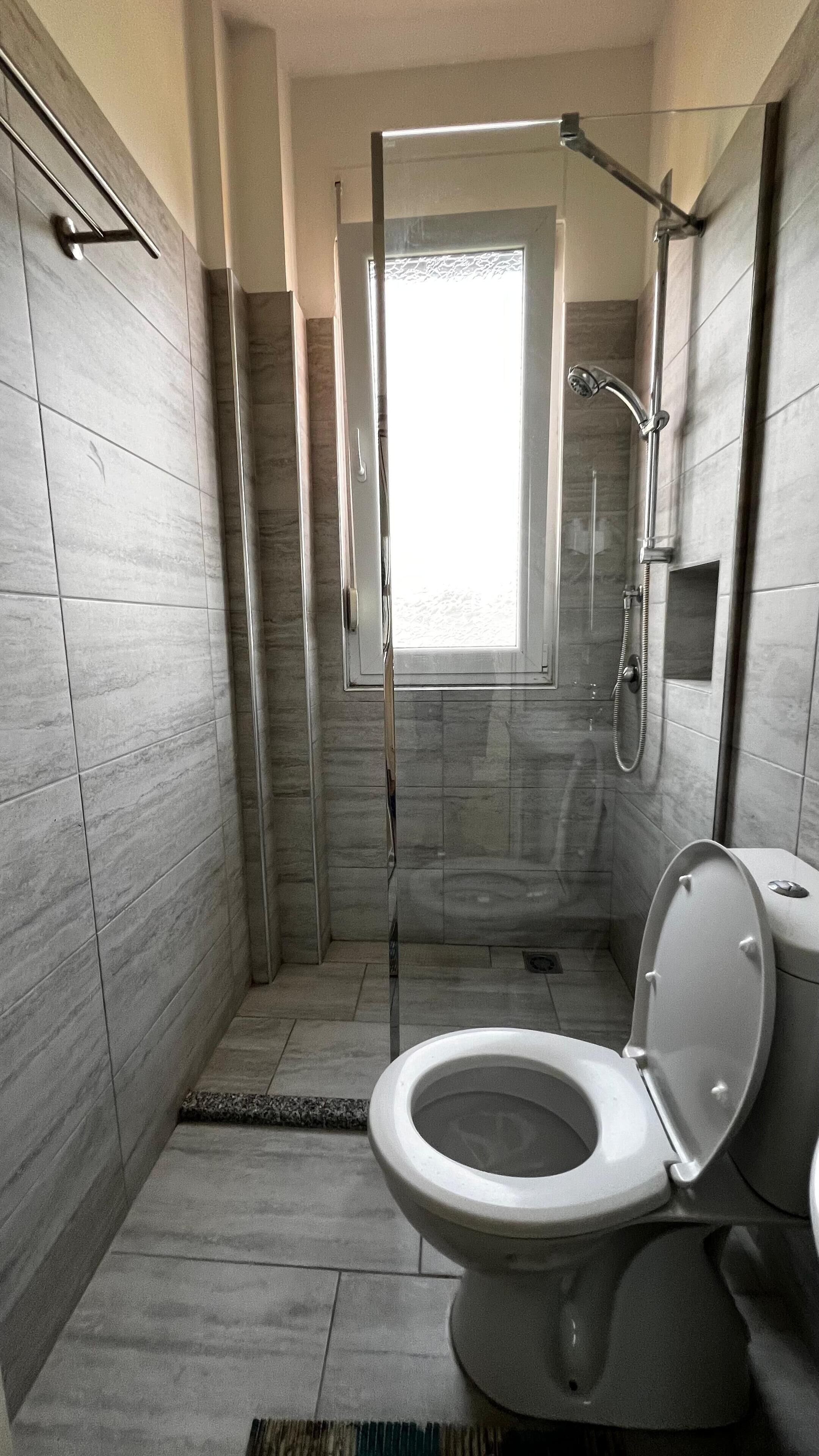 A modern bathroom with a glass-enclosed shower, a toilet, and a window providing natural light.