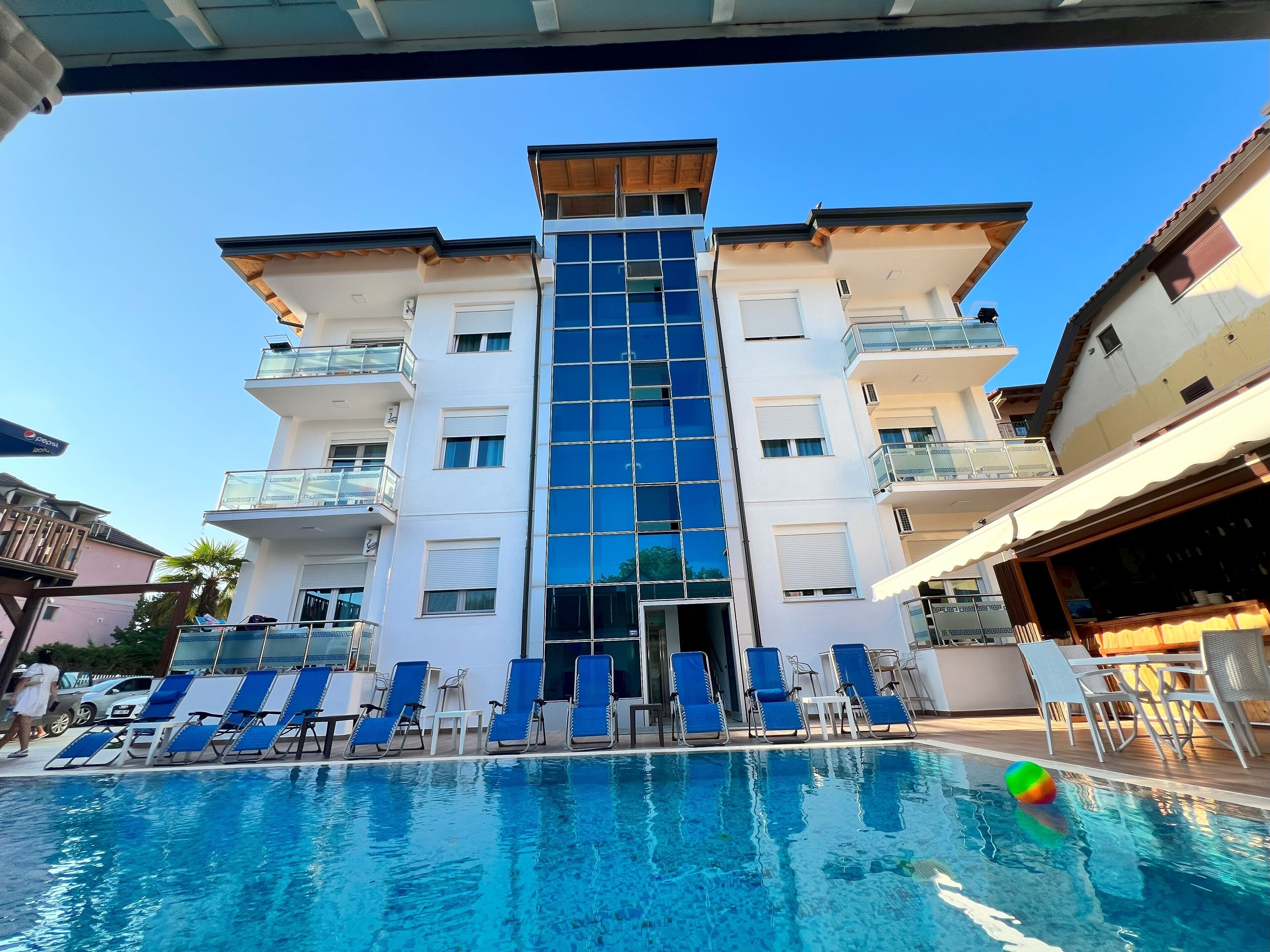 Un hotel con piscina, sillas de descanso azules y una fachada de edificio moderna.