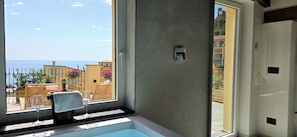 A bathroom with a bathtub, a window with a view of the sea, and a towel rack with a towel. - Cinqueterrehomes (Riomaggiore)