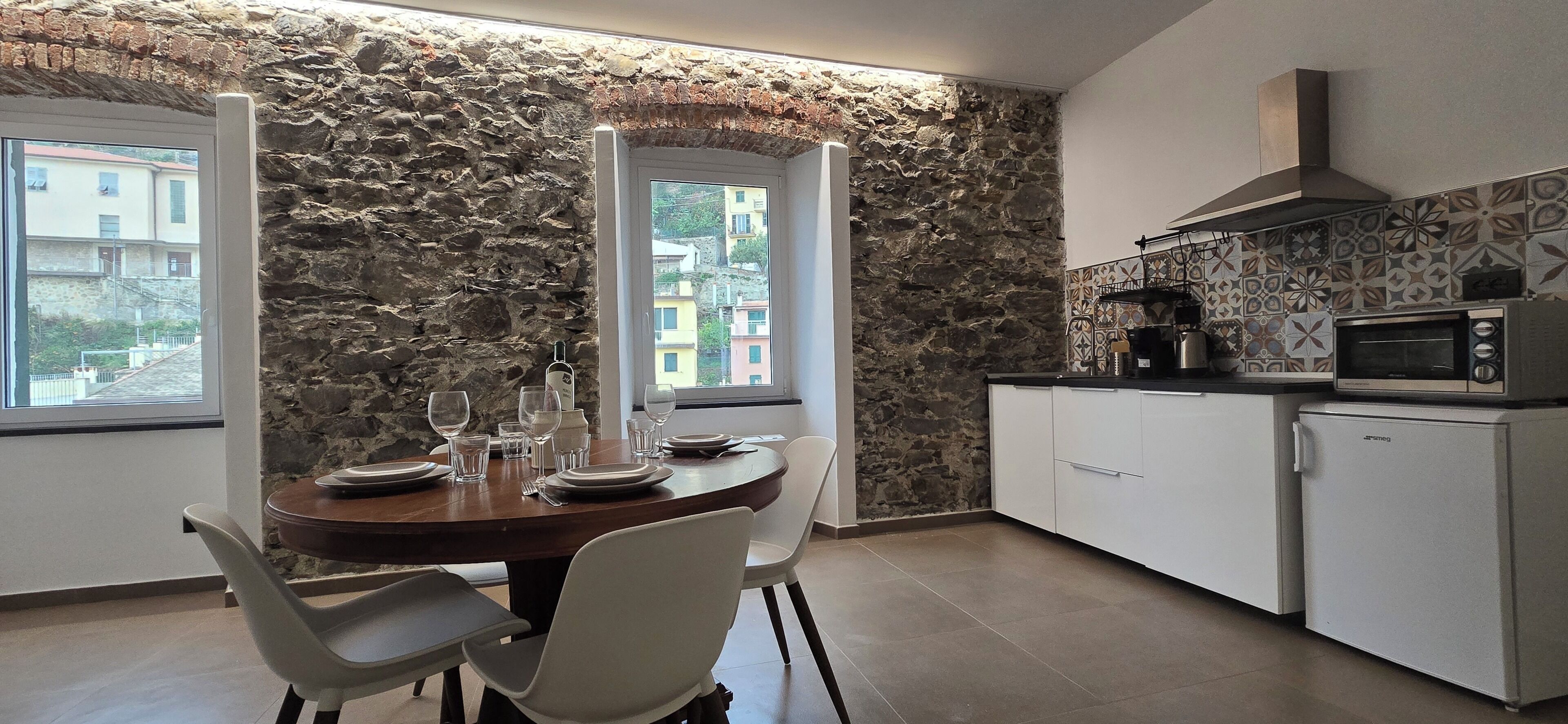 A modern kitchen with stone walls, a dining table set for four, and a view of buildings through a window.