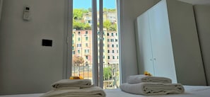 A hotel room with a bed, a window with a view of buildings, and a wall-mounted thermostat. - Cinqueterrehomes (Riomaggiore)