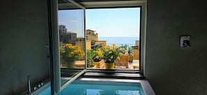 Casa de banho com banheira, janela vista para o mar e plantas em vasos.
