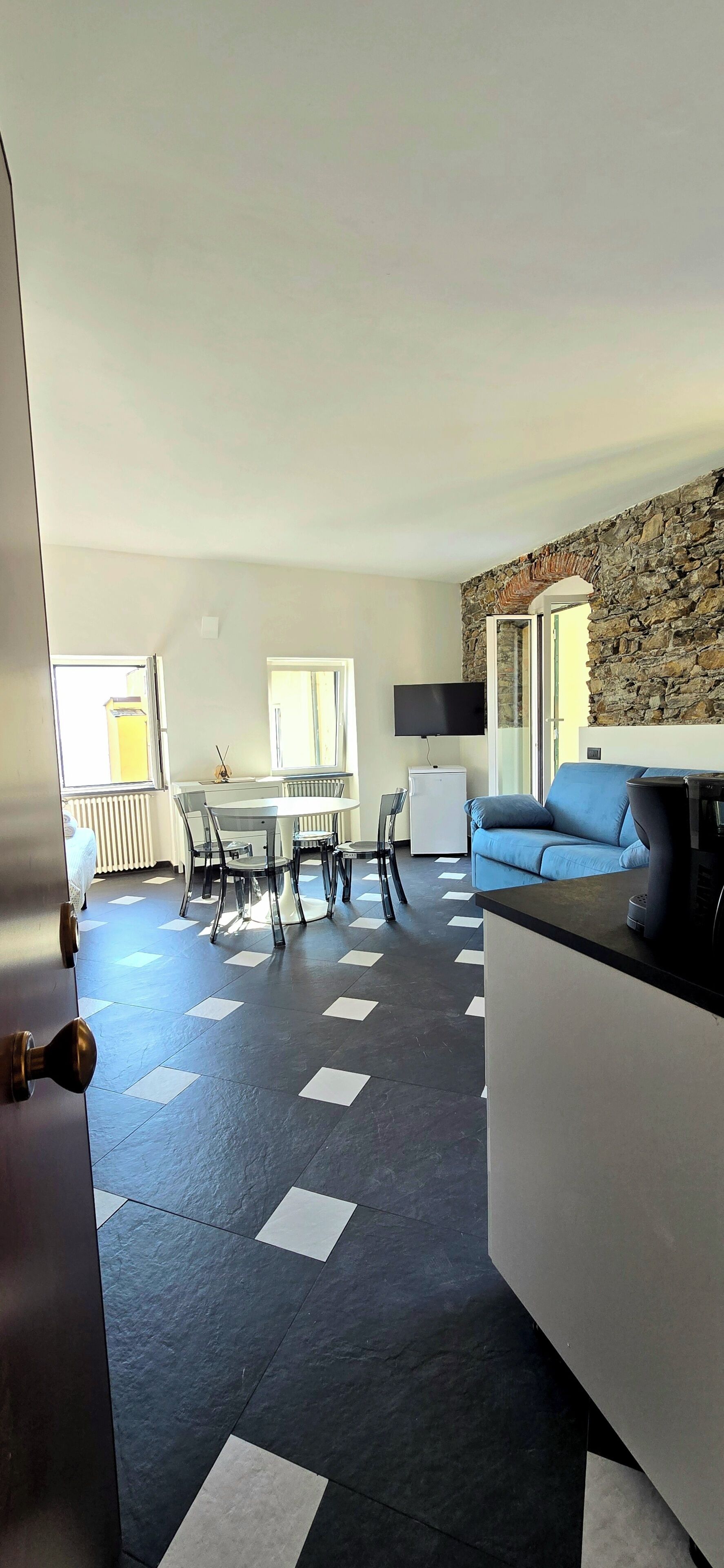 A modern living room with a stone accent wall, a blue sofa, a coffee machine, and a dining area with a table and chairs.