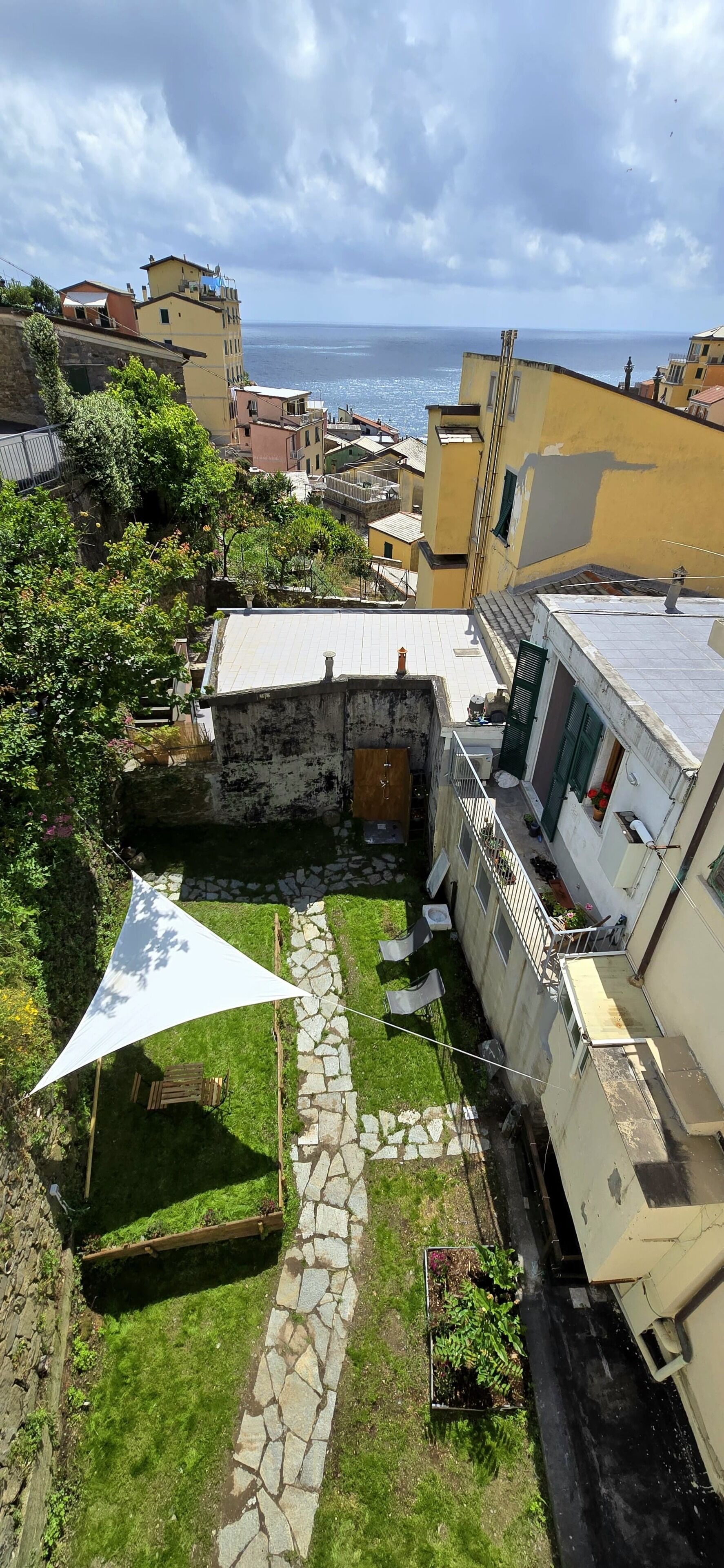 A courtyard with a stone pathway, a white triangular shade, and a view of the sea.