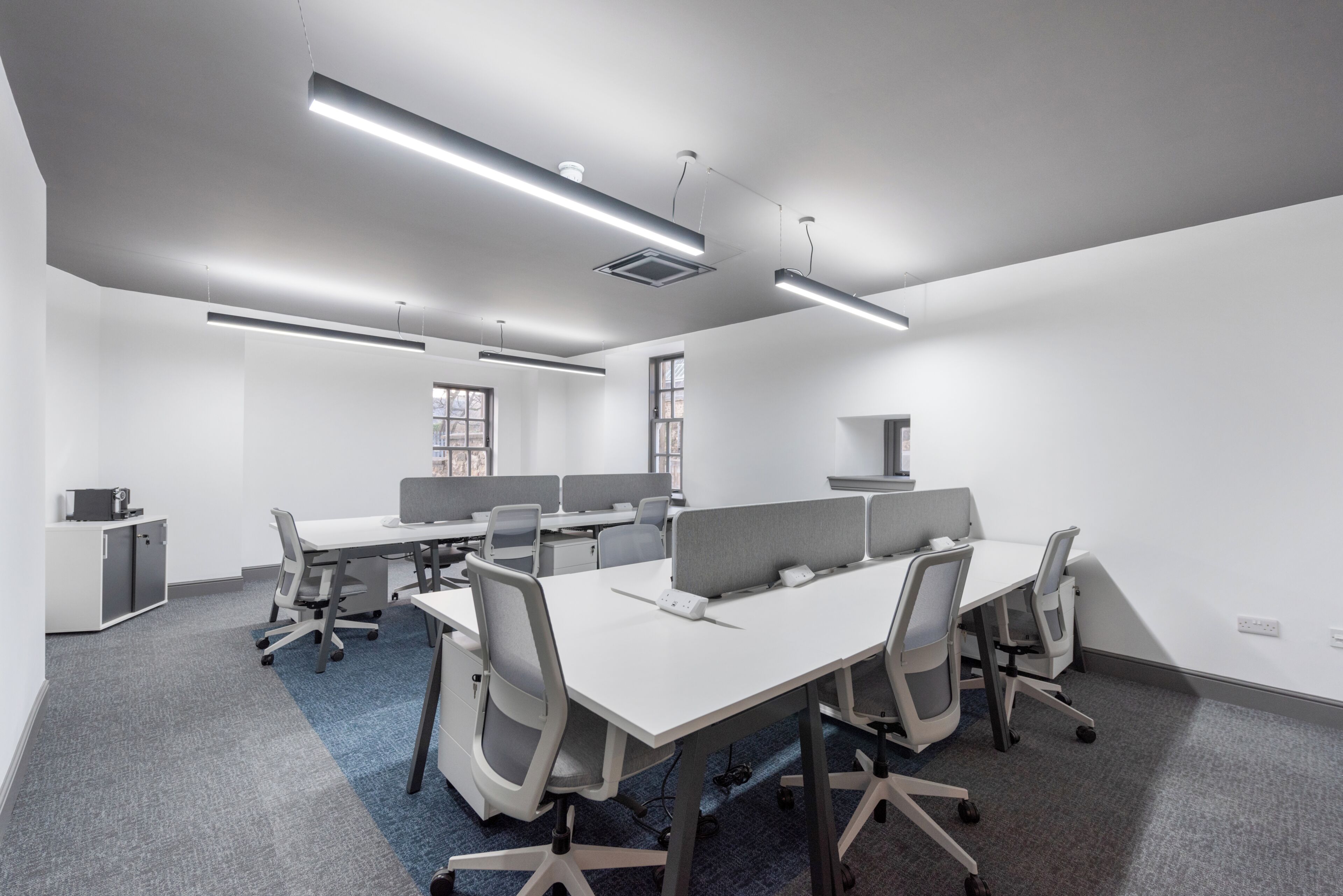 A modern conference room with white tables, grey chairs, and overhead lighting.
