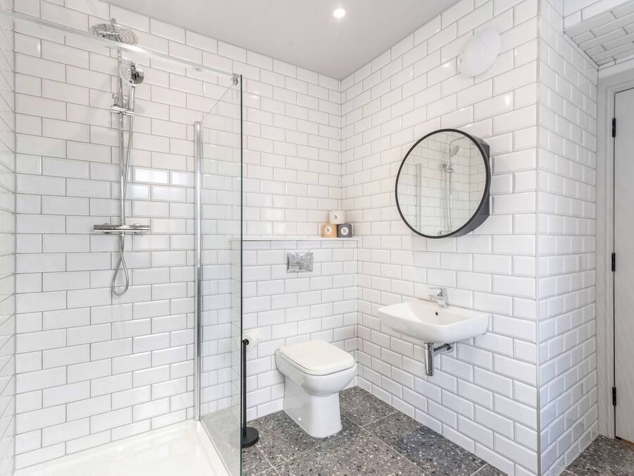 A modern bathroom with white subway tiles, a glass-enclosed shower, a toilet, and a sink with a round mirror.