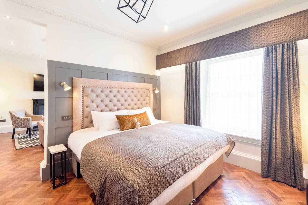 A modern bedroom with a tufted headboard, a large bed, a bedside table, and a chair.