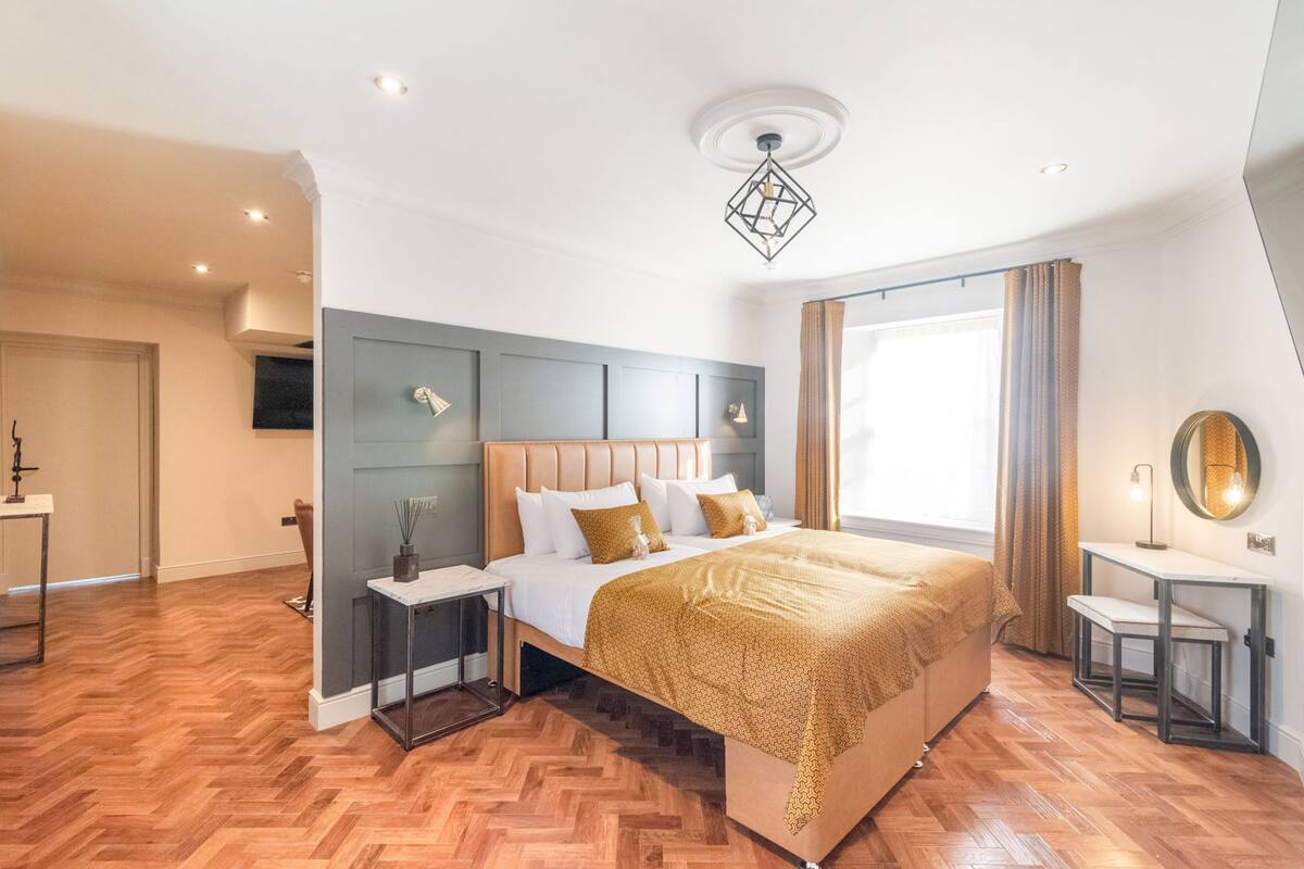 A modern bedroom with a large bed, a bedside table, a nightstand, a mirror, and a window with curtains.