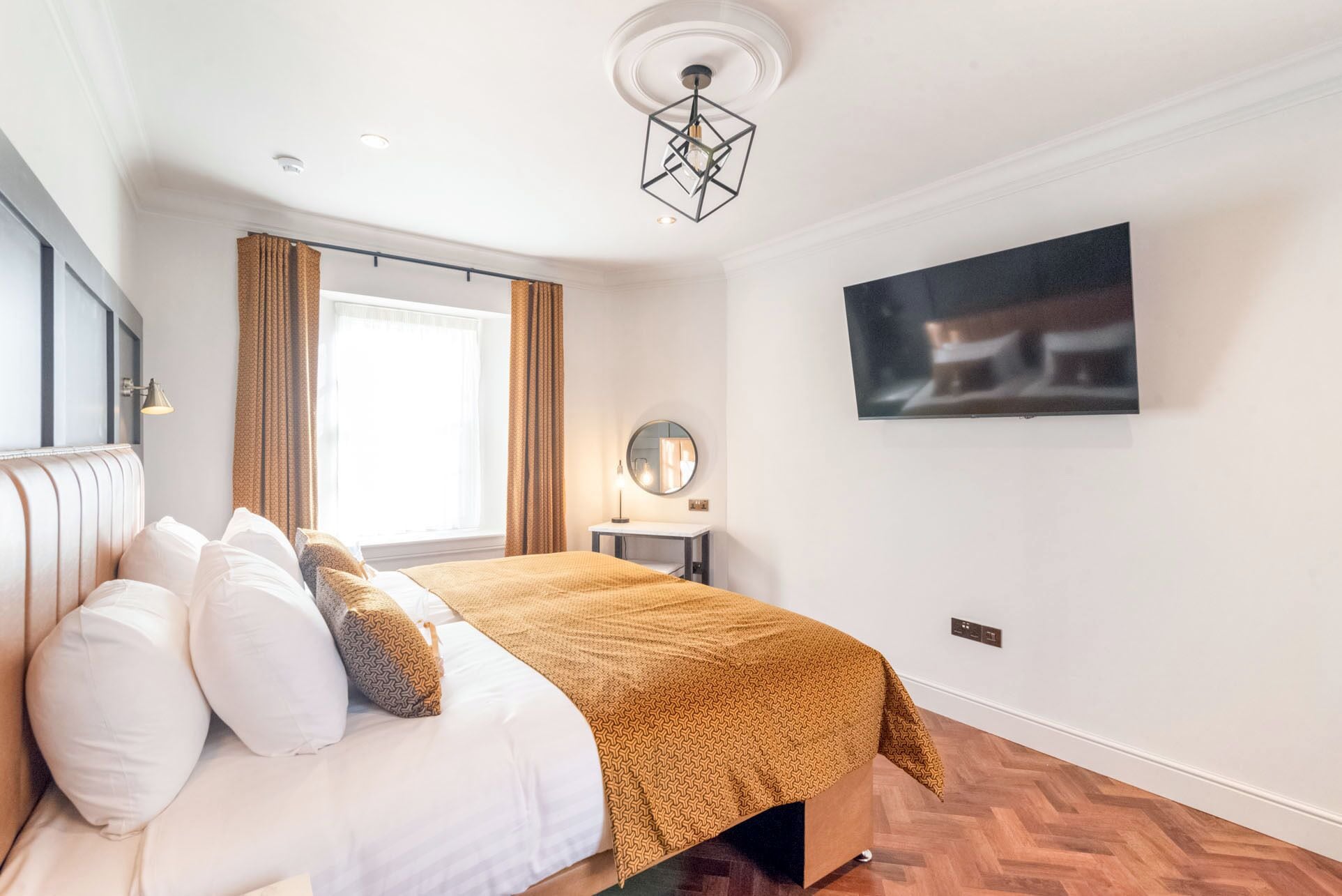 A modern bedroom with a bed, a bedside table, a mirror, and a wall-mounted TV.