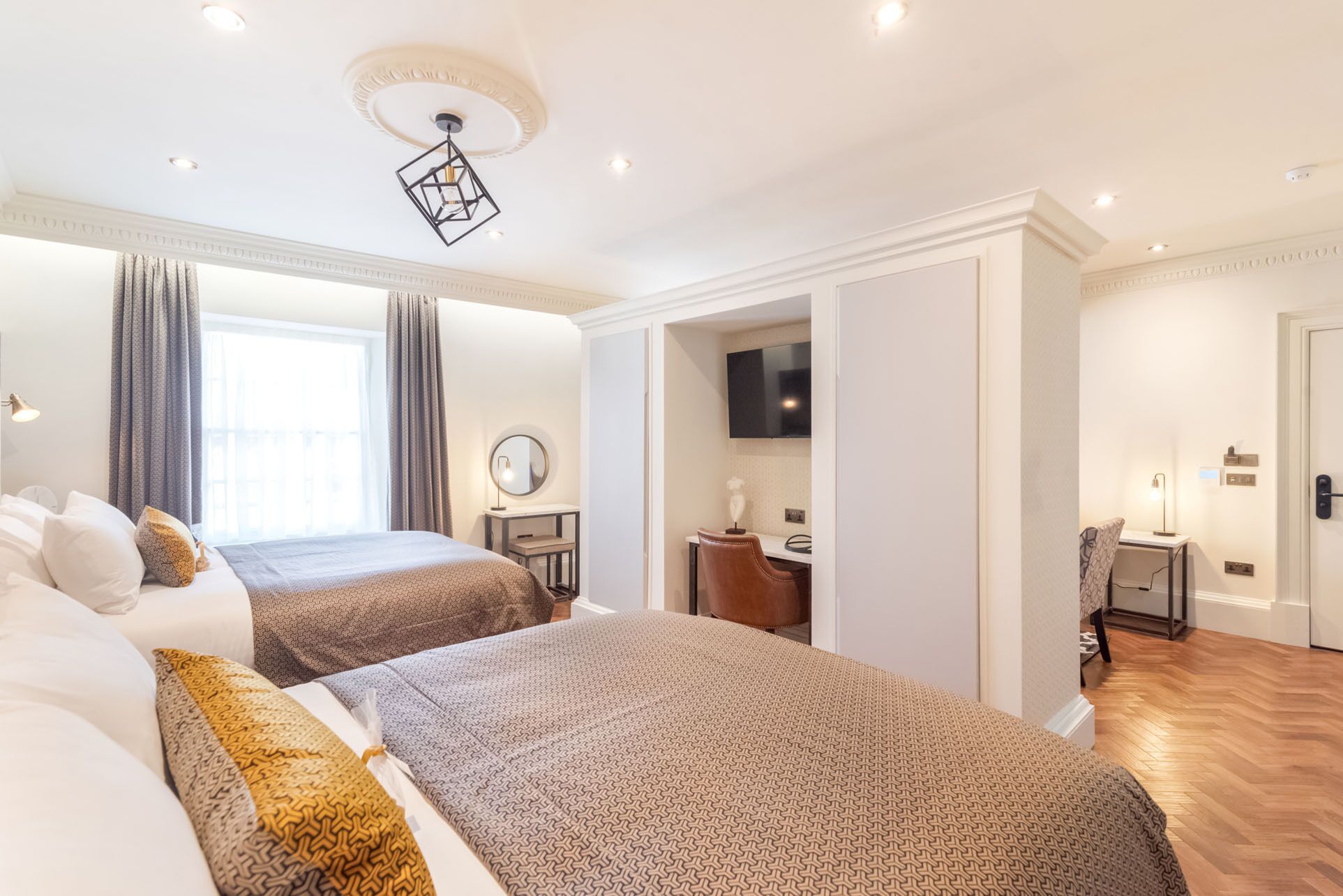 A hotel room with two beds, a TV, a desk, and a mirror.