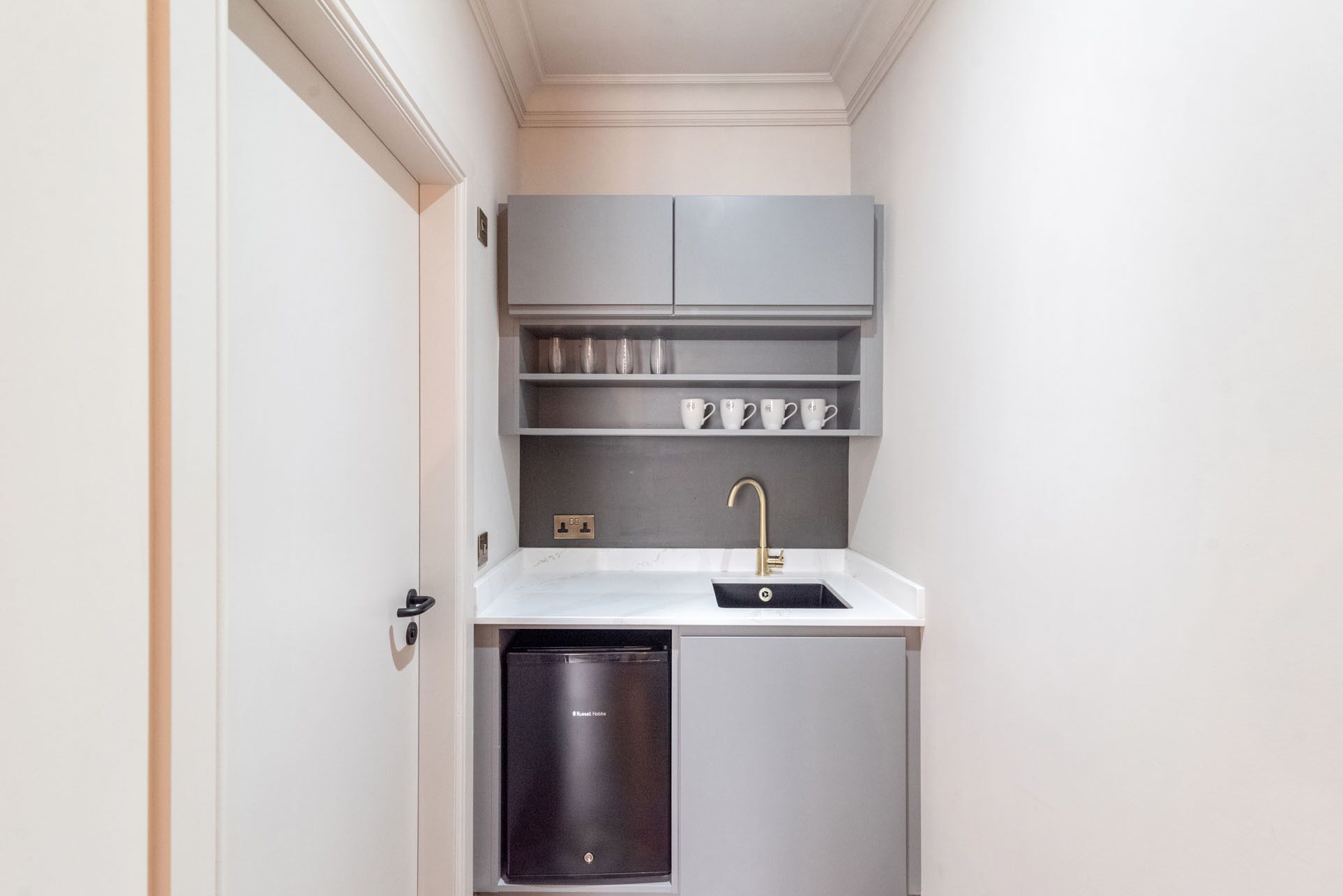 Une petite cuisine équipée, avec un lave-vaisselle intégré, un évier et des étagères au-dessus pour le rangement.