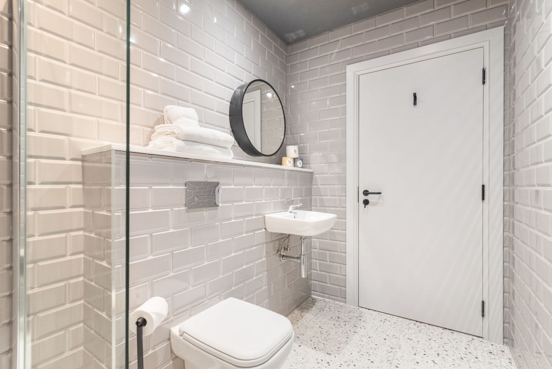 Een badkamer met witte metrotegels, een wit toilet, een douchecabine van glas, een witte wasbak en een witte deur.