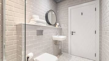 Een badkamer met witte metrotegels, een wit toilet, een douchecabine van glas, een witte wasbak en een witte deur.