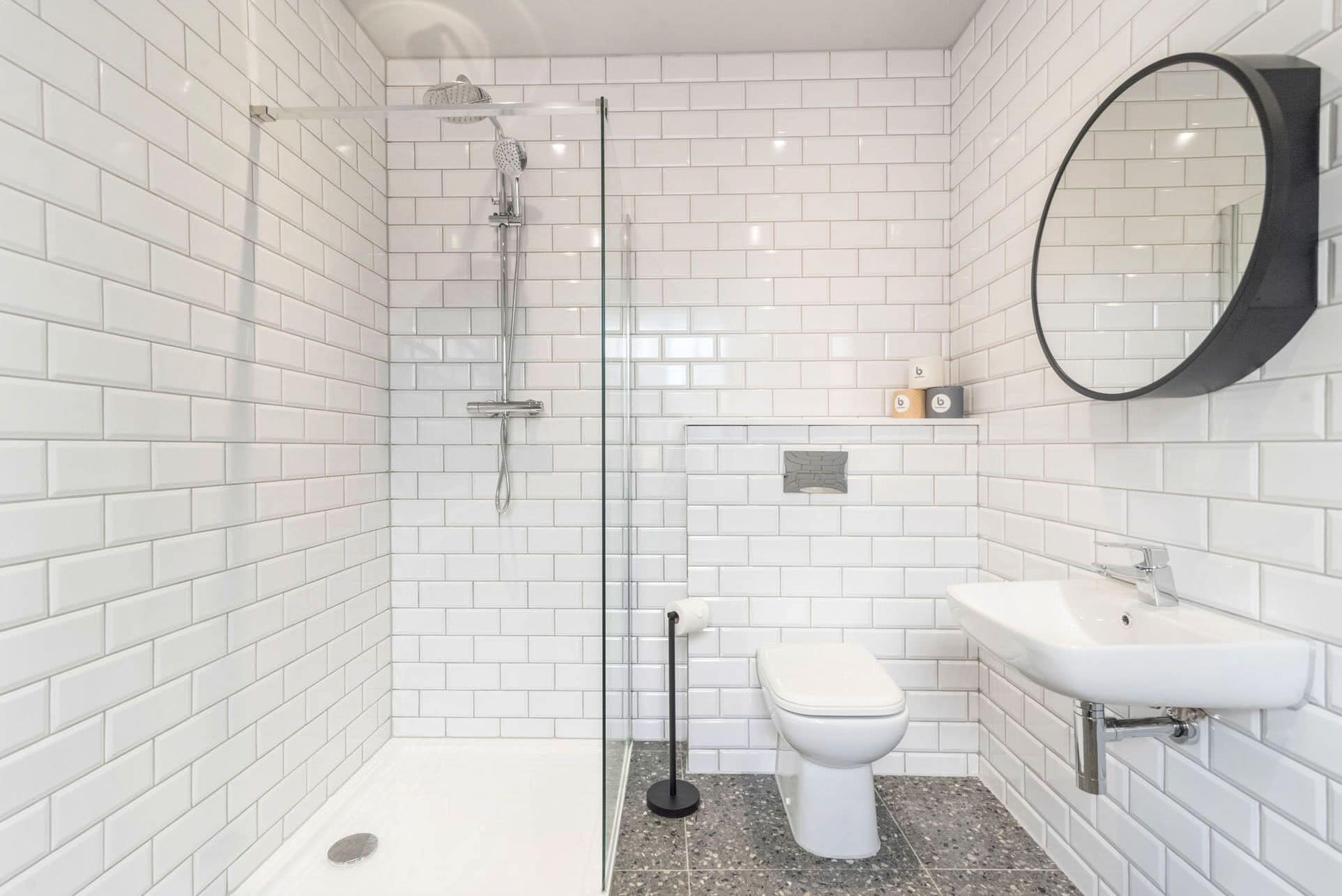 A modern bathroom with white subway tiles, a glass-enclosed shower, a toilet, and a sink with a mirror.