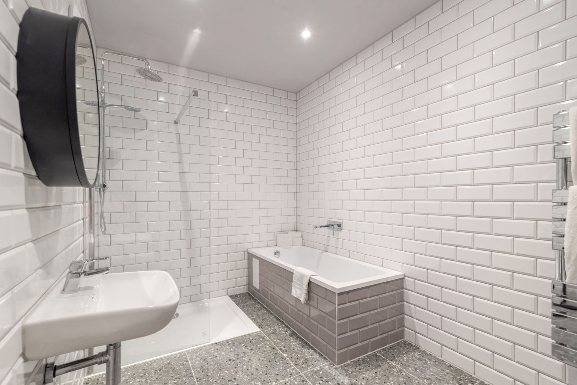 Un baño moderno con azulejos blancos tipo metro, un lavamanos blanco, una bañera y una ducha.