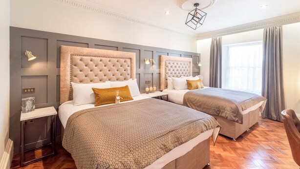 A hotel room with two beds, a modern chandelier, and a large window with curtains. - King Street Aparthotel (Stirling)
