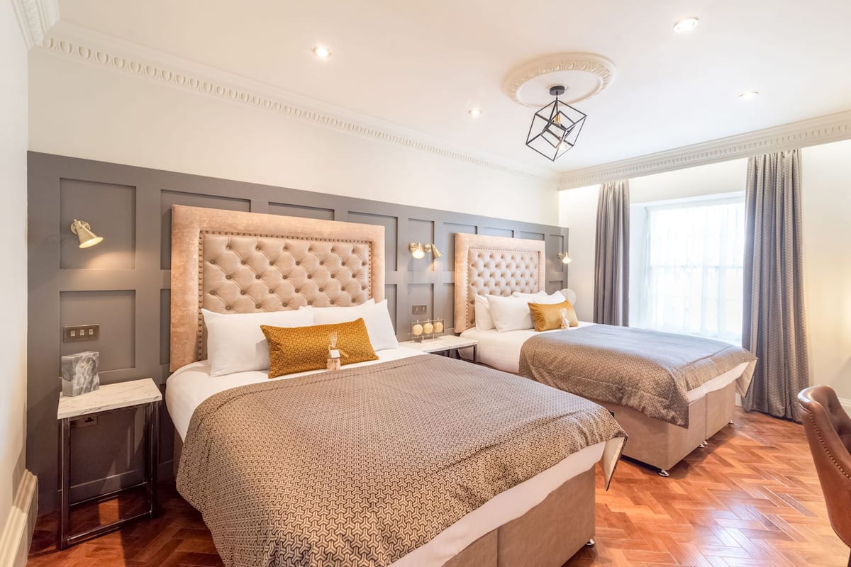 A hotel room with two beds, a modern chandelier, and a large window with curtains.