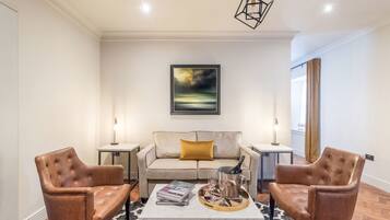 A modern living room with a sofa, two armchairs, a coffee table, and a painting on the wall.