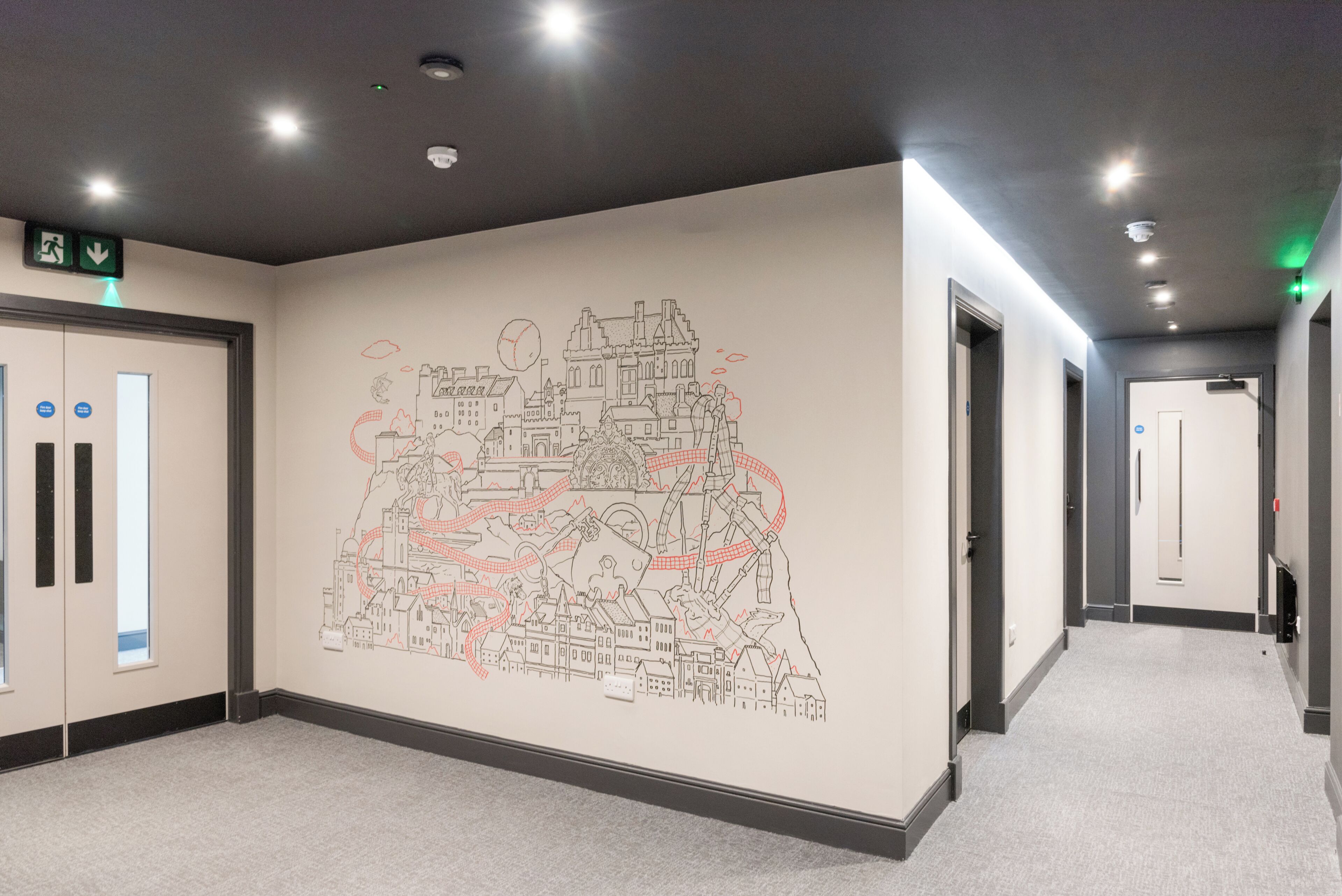 A hallway with a large wall mural depicting a cityscape, doors, and emergency exit signs.