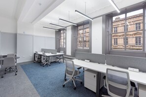 A modern office space with cubicles, desks, chairs, and large windows offering views of buildings. - King Street Aparthotel (Stirling)