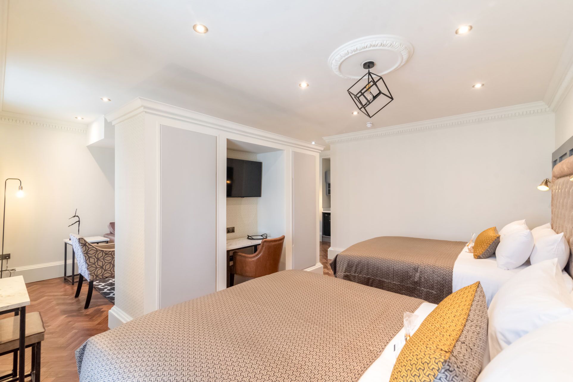 A hotel room with two beds, a desk, and a chair. There is a television on the wall and a ceiling light fixture.