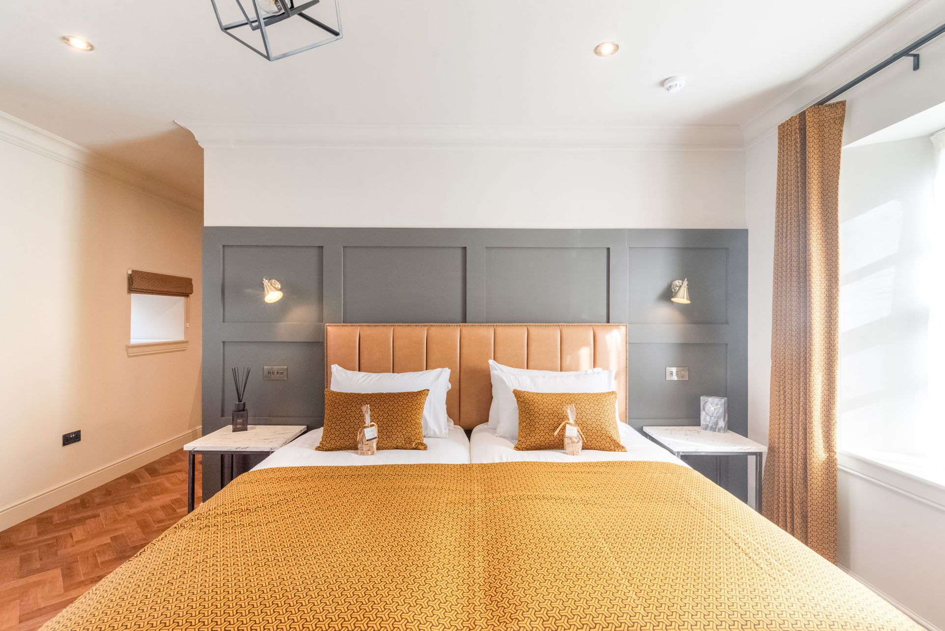 A hotel room with a large bed, two bedside tables, a headboard, and a window with curtains.