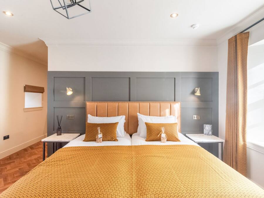 A hotel room with a large bed, two bedside tables, a headboard, and a window with curtains.