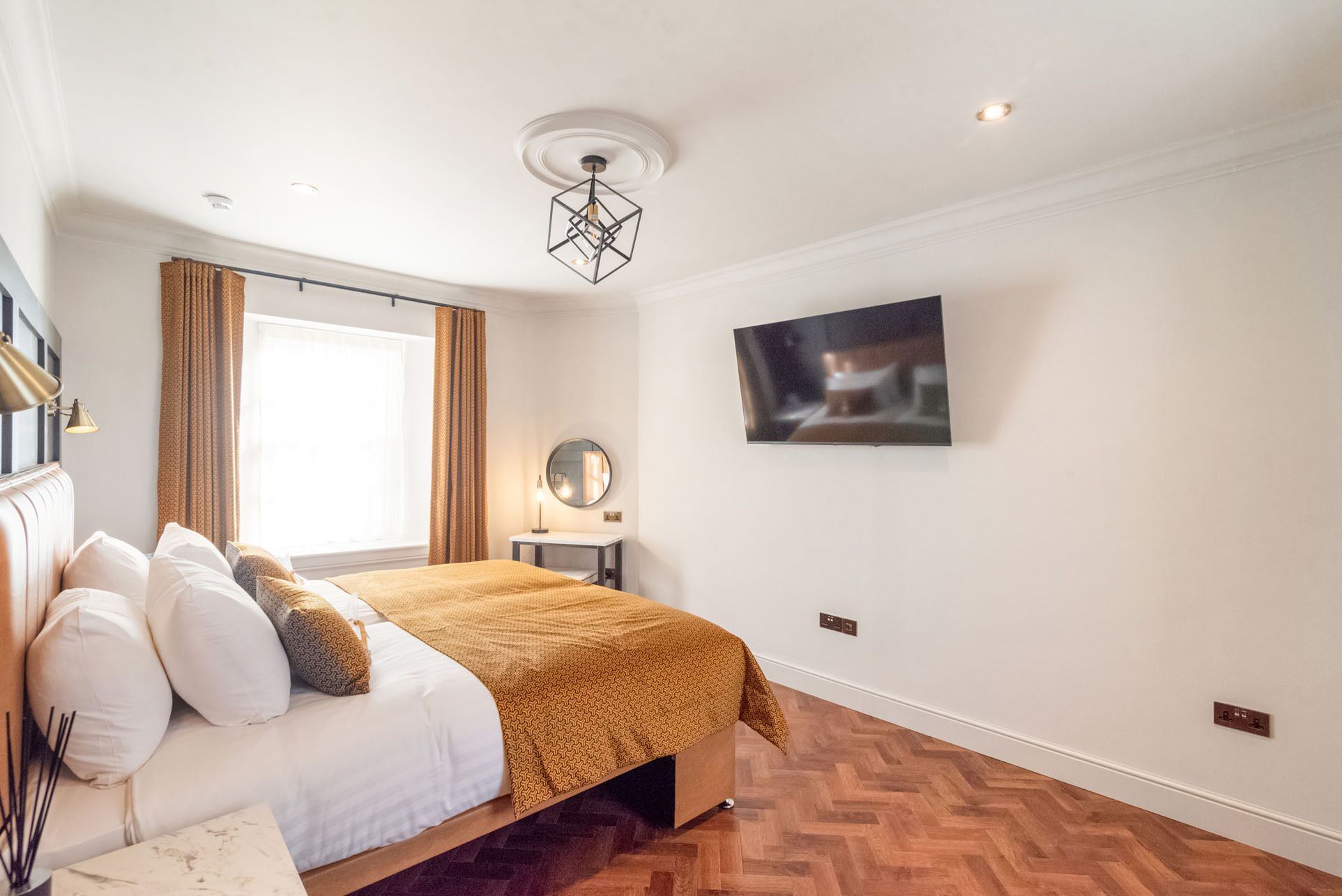 Une chambre à coucher moderne avec un lit, une télévision, un miroir et une fenêtre avec des rideaux.
