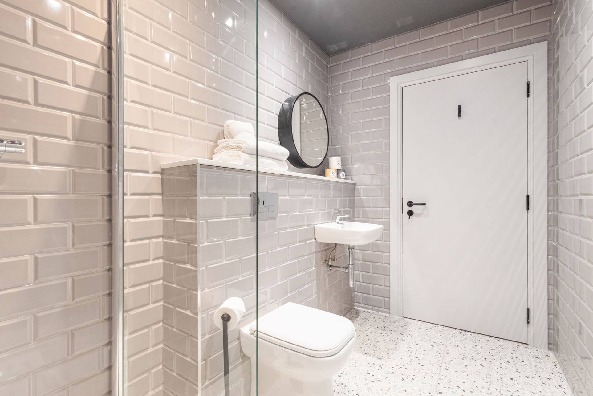 Un baño con azulejos blancos estilo metro, cabina de ducha de vidrio, inodoro, lavabo y puerta.