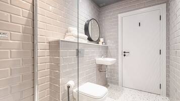 Un baño con azulejos blancos estilo metro, cabina de ducha de vidrio, inodoro, lavabo y puerta.
