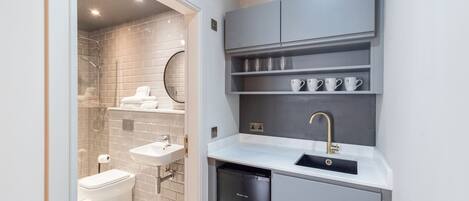 A compact bathroom with a glass shower enclosure, a toilet, a sink with a modern faucet, and a built-in dishwasher.