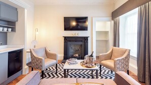 A modern living room with a fireplace, two armchairs, a coffee table with magazines and a champagne bottle, and a TV mounted above the fireplace. - King Street Aparthotel (Stirling)