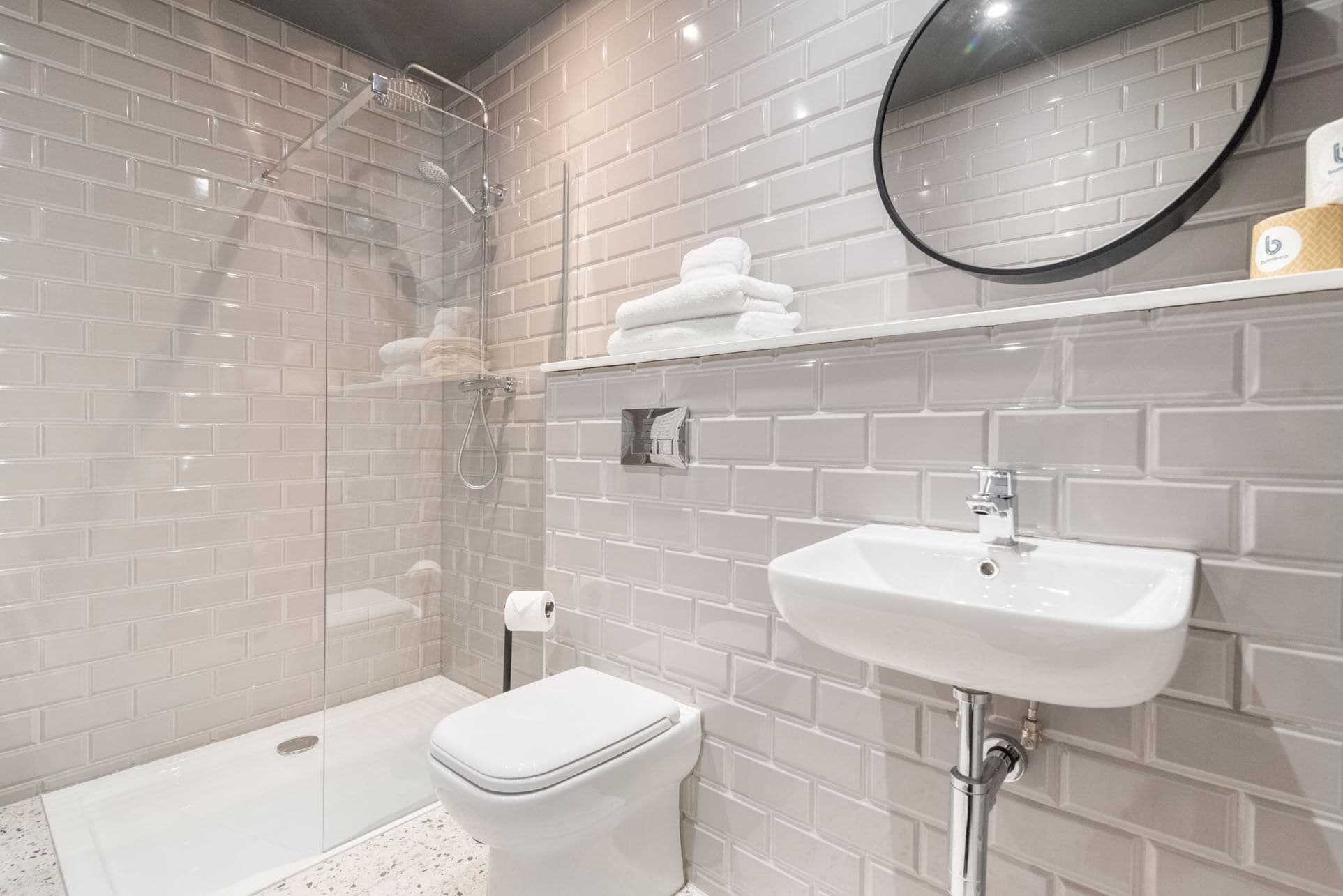 Un baño moderno con ducha de vidrio, inodoro blanco y lavamanos con espejo.