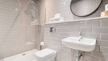 A modern bathroom with a glass-enclosed shower, a white toilet, and a sink with a mirror above it.