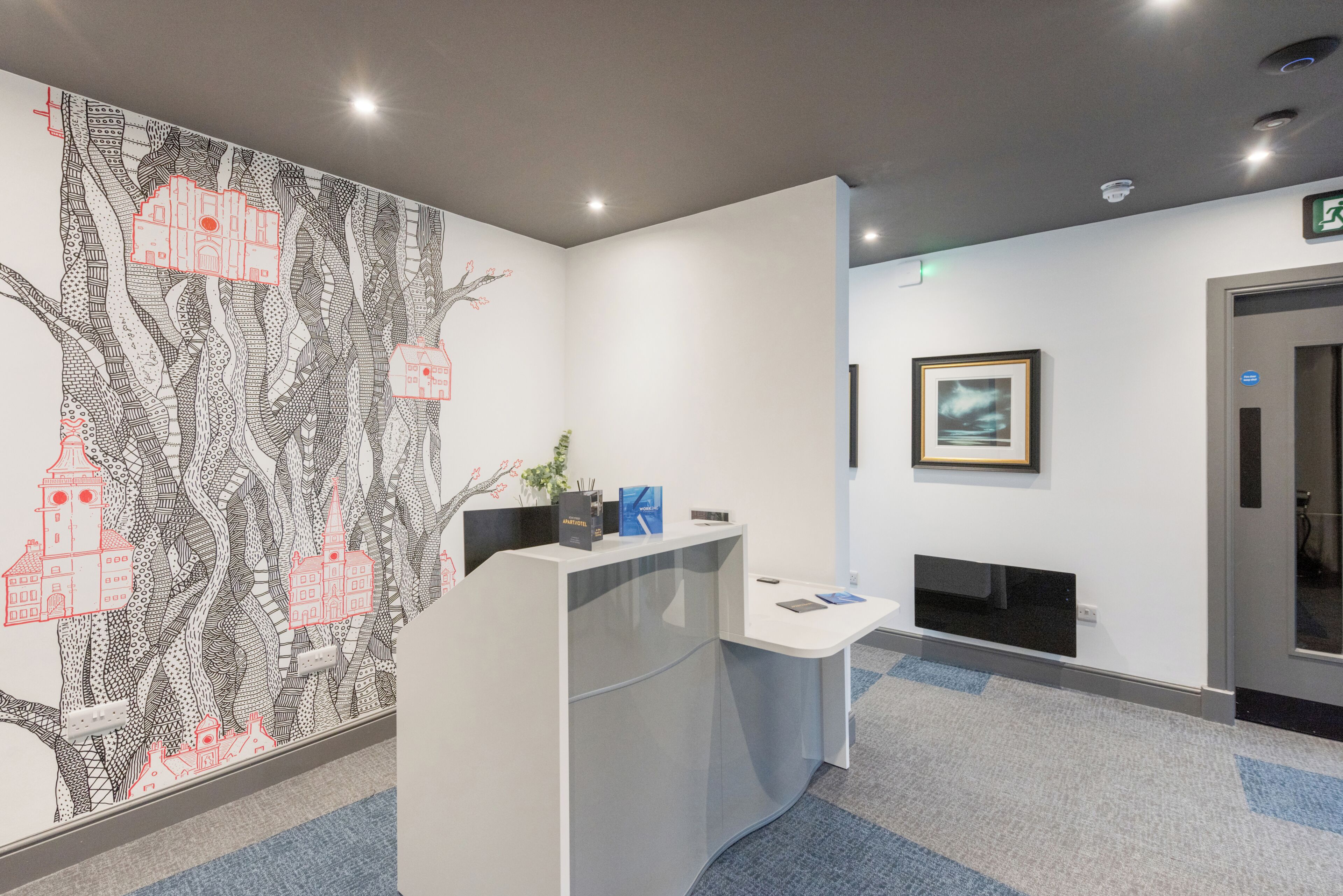 A reception desk with a patterned wall mural, a framed picture, and a carpeted floor.