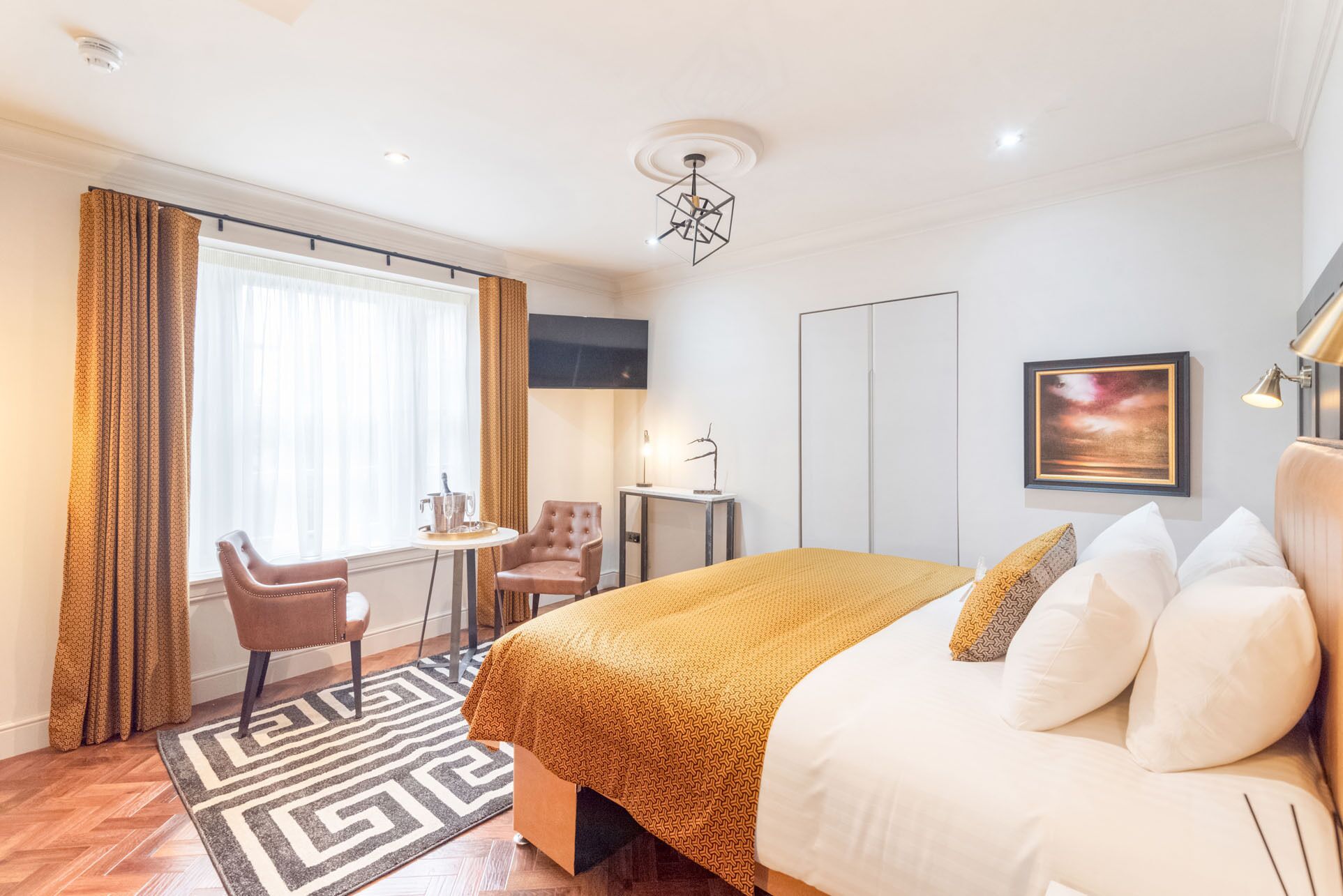 Una habitación de hotel con una cama grande, un escritorio con silla, un televisor montado en la pared y un ventanal con cortinas.