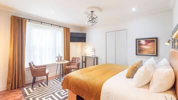 Una habitación de hotel con una cama grande, un escritorio con silla, un televisor montado en la pared y un ventanal con cortinas.