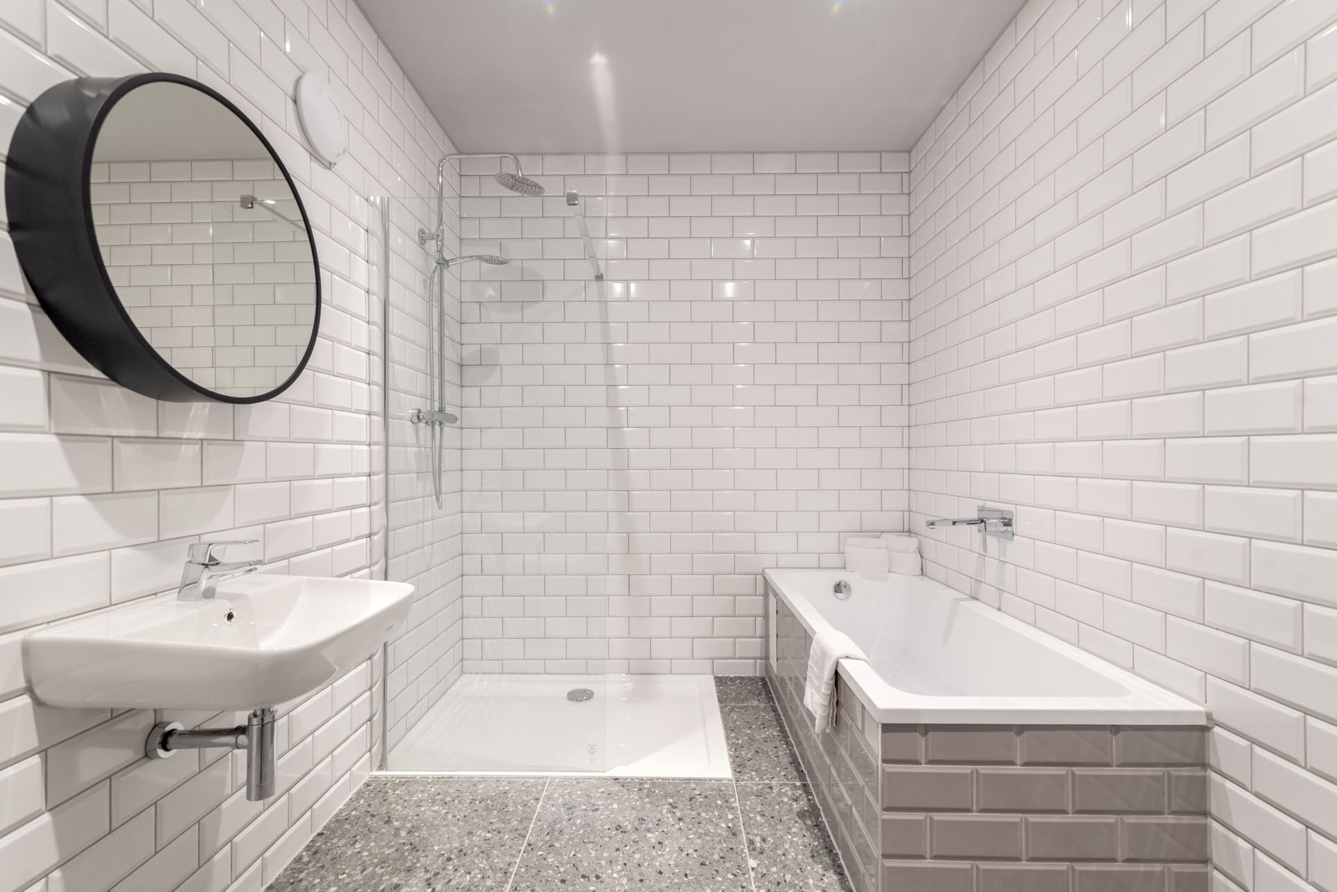 A modern bathroom with white subway tiles, a round mirror, a shower, a sink, and a bathtub.