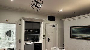 A modern kitchen with white cabinetry, a dishwasher, and a built-in oven. There is a seating area with a sofa and a coffee table. - King Street Aparthotel (Stirling)