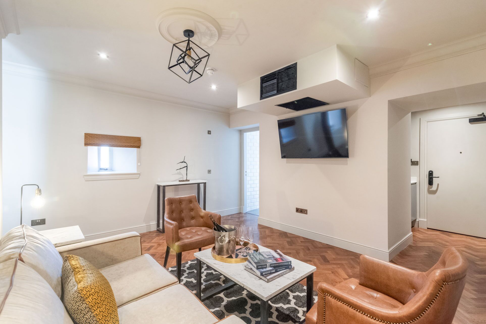 A modern living room with a sofa, armchairs, a coffee table, and a TV mounted on the wall.