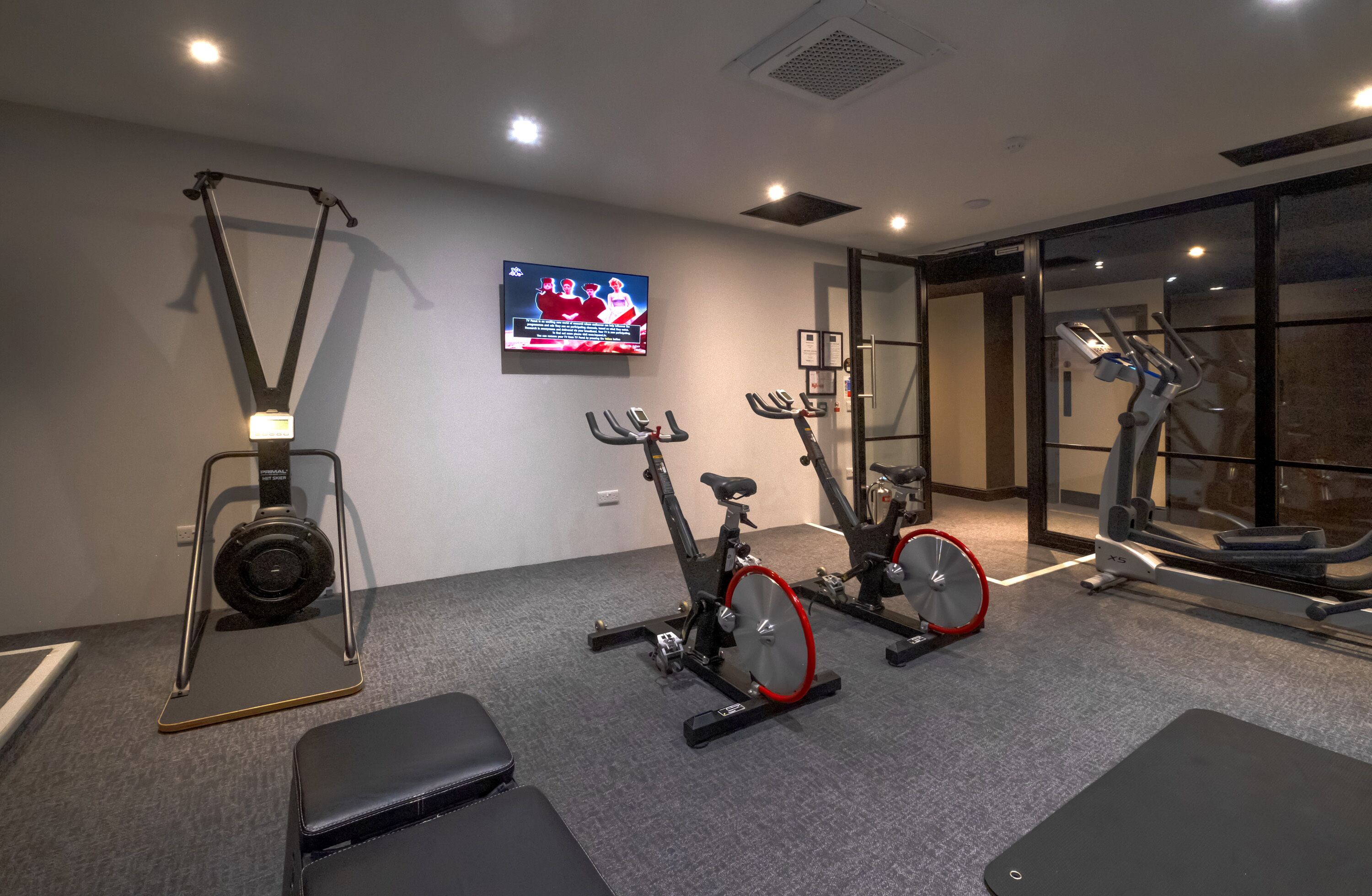 A gym with stationary bikes, a treadmill, and a television displaying a sports event.