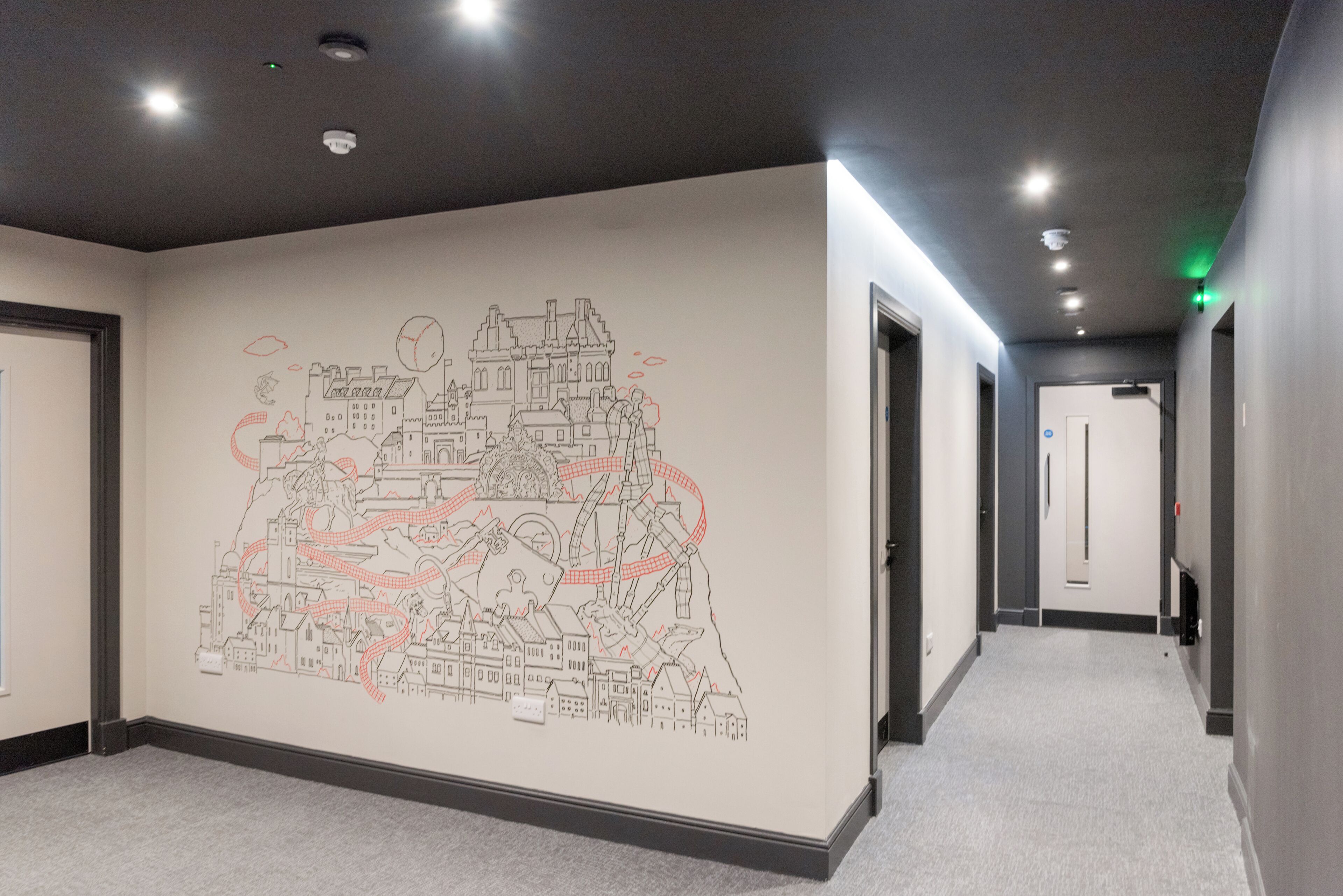 A hallway with a wall mural depicting a cityscape, doors on both sides, and a carpeted floor.