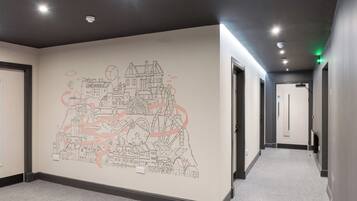 A hallway with a wall mural depicting a cityscape, doors on both sides, and a carpeted floor.